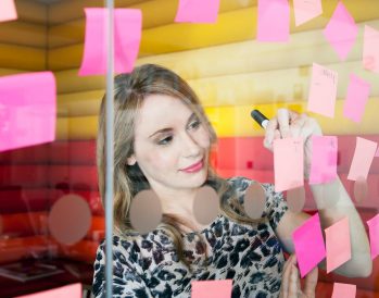 woman writing on post it notes hanging on glass wall