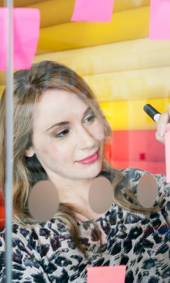 woman writing on post it notes hanging on glass wall