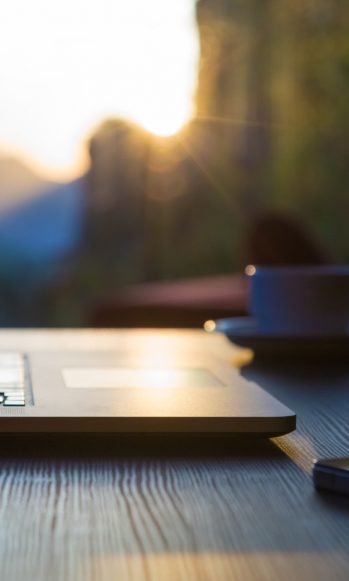 Computer and coffee cup on table. Blurred out mountains in background.
