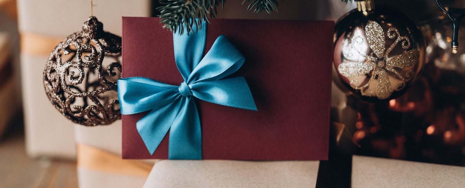 Gift voucher in burgundy envelope with blue bow under the Christmas tree. Increasing Gift Card Sales This Holiday Season