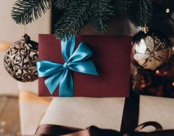 Gift voucher in burgundy envelope with blue bow under the Christmas tree. Increasing Gift Card Sales This Holiday Season