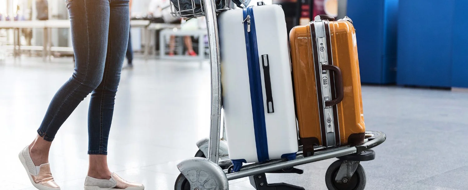 Female person is walking through airport-foyer with her luggage at small cart. Focus on baggage. Close up of her legs