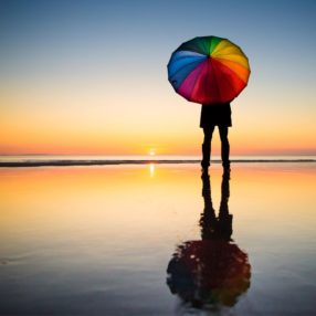 mutli-colored beach umbrella being held by a person on the beach at sunrise